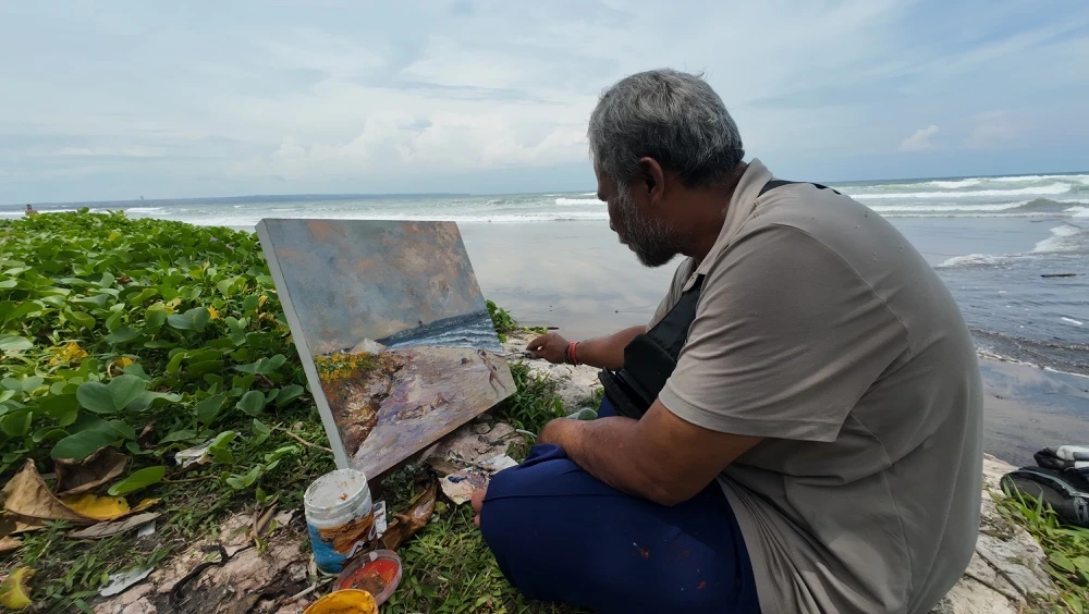 Painting the Spirit of Bali Beneath the Seminyak Sun - Arts of Bali A Balinese artist sitting on the sand while painting a beautiful ocean landscape on canvas at Seminyak Beach