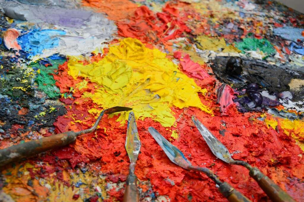 Close-up of a colorful artist's palette with spatulas and vibrant mixed paints.