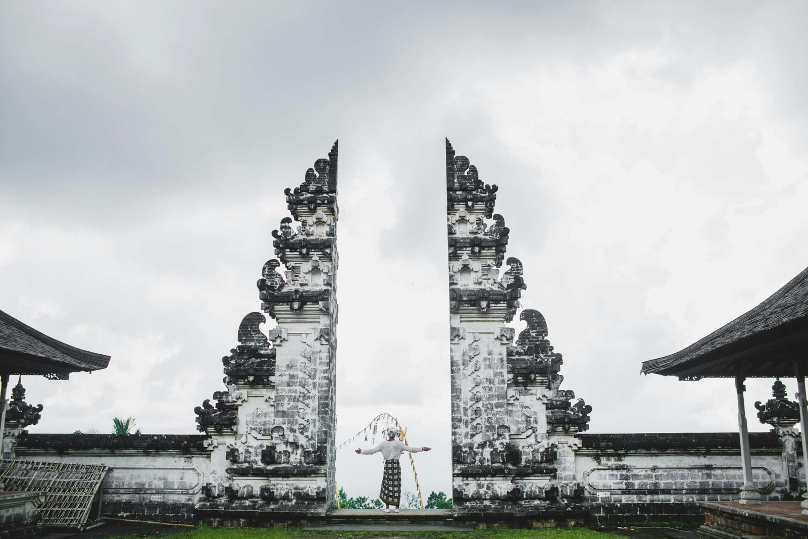 A person stands between the iconic Gates of Heaven at Lempuyang Temple, Bali, under a cloudy sky.