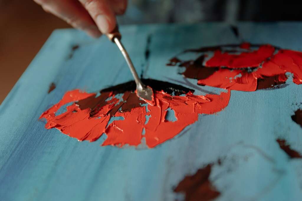 Close-up of a palette knife applying thick paint on a blue canvas.
