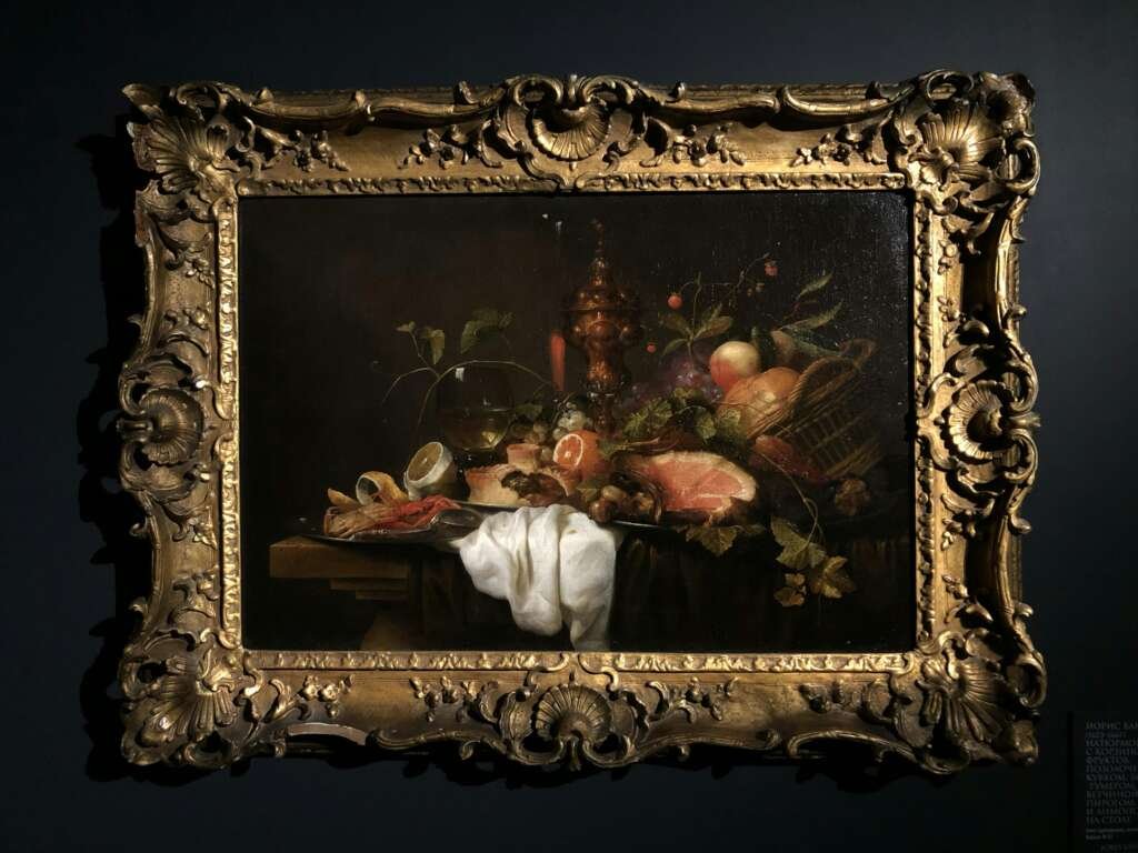 Decorative framed still life oil painting featuring fruits and objects, showcased indoors.