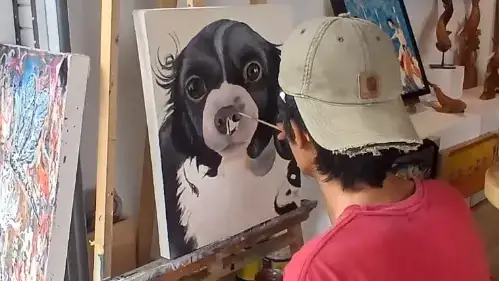 Alzen the lead artist at Arts of Bali painting a realistic black and white dog portrait on canvas.