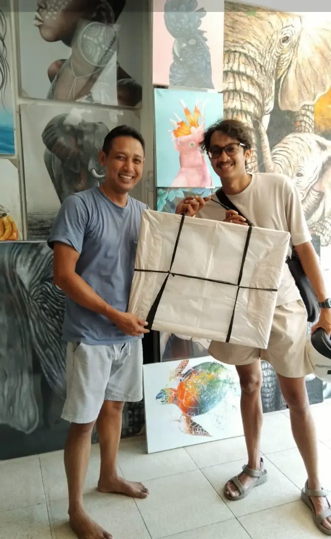 Bali painting souvenir packed and ready to go — Arts of Bali A happy buyer holding a securely wrapped canvas painting as bali painting souvenir to take home from Arts of Bali gallery Seminyak Bali