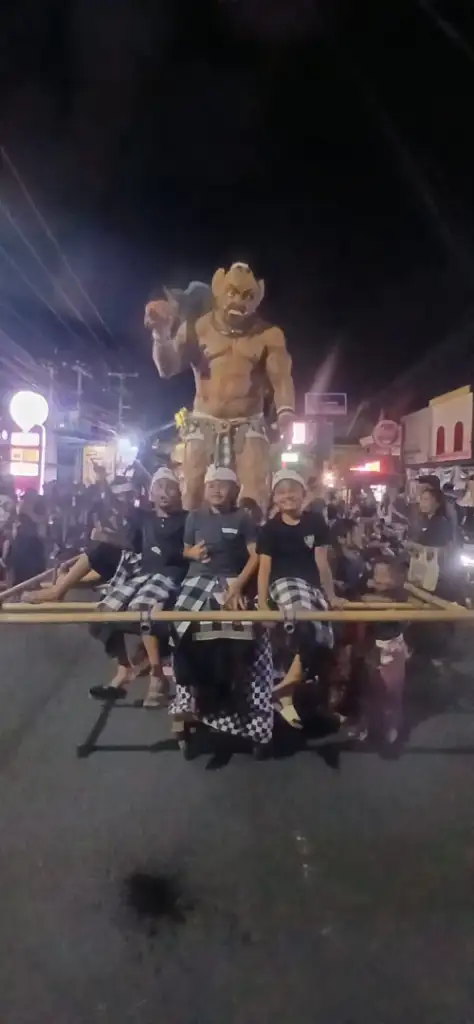 From the Noise to the Silence: Nyepi with the Arts of Bali Family - Arts of Bali Young boys in black and white Balinese attire sitting beneath their handmade ogoh-ogoh demon figure during the night parade before Nyepi
