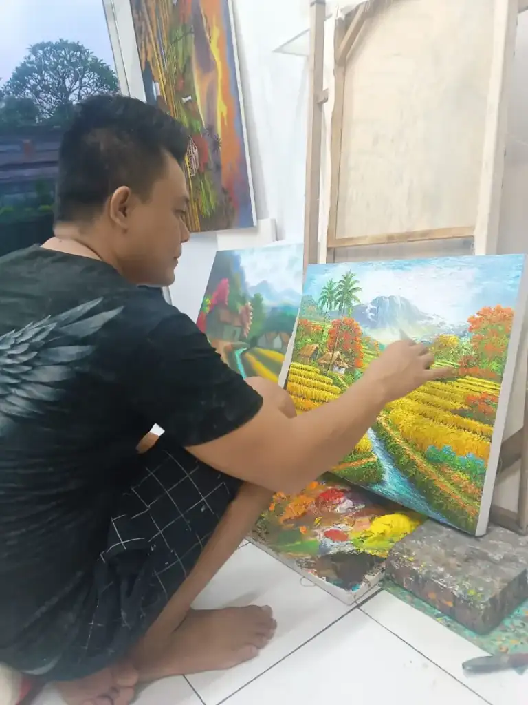 A.Gandara: The Man Who Found Himself in the Texture of the Land - Arts of Bali Balinese artist A. Gandara adding detail to rice field village landscape painting in studio