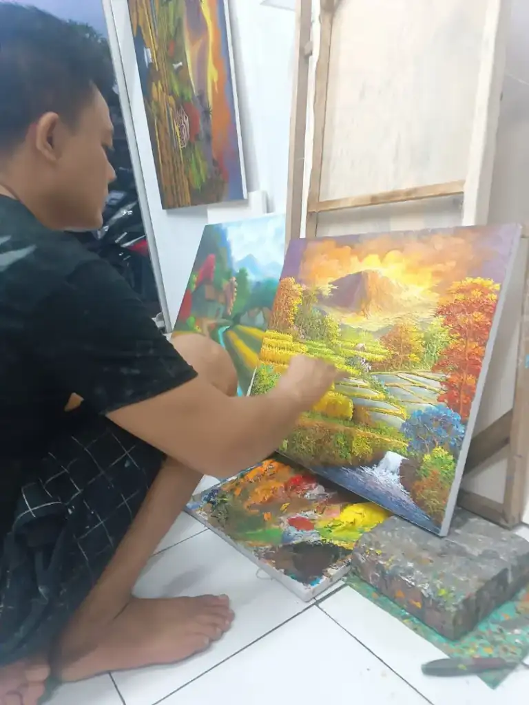 A.Gandara: The Man Who Found Himself in the Texture of the Land - Arts of Bali Balinese artist A. Gandara working on dramatic golden volcano sunset landscape painting in Arts of Bali studio Seminyak