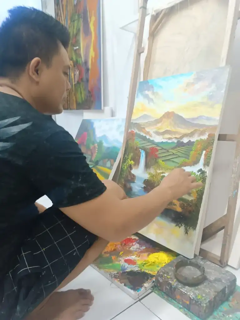 A.Gandara: The Man Who Found Himself in the Texture of the Land - Arts of Bali A. Gandara applying paint to volcano and waterfall landscape canvas in studio
