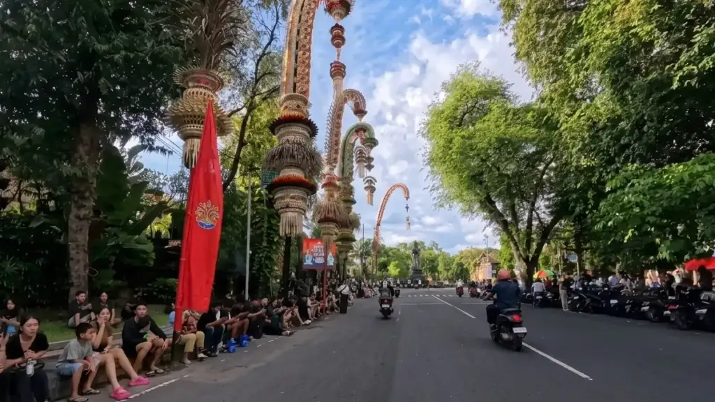 From the Noise to the Silence: Nyepi with the Arts of Bali Family - Arts of Bali Penjor decorations lining a busy Balinese street as crowds gather on the sidewalk the evening before Nyepi