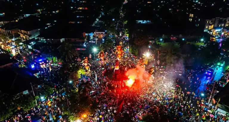 Drone aerial photograph of a massive Nyepi eve parade in Bali showing giant ogoh-ogoh figures, fire, and tens of thousands of people filling the streets at night