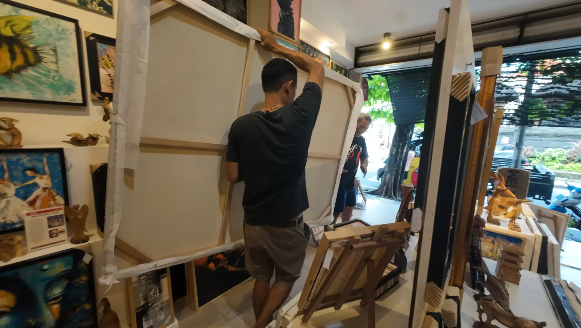Packing a large painting for safe transport — Arts of Bali Seminyak Arts of Bali staff carefully wrapping a large canvas painting in protective material for transport at the gallery entrance in Seminyak