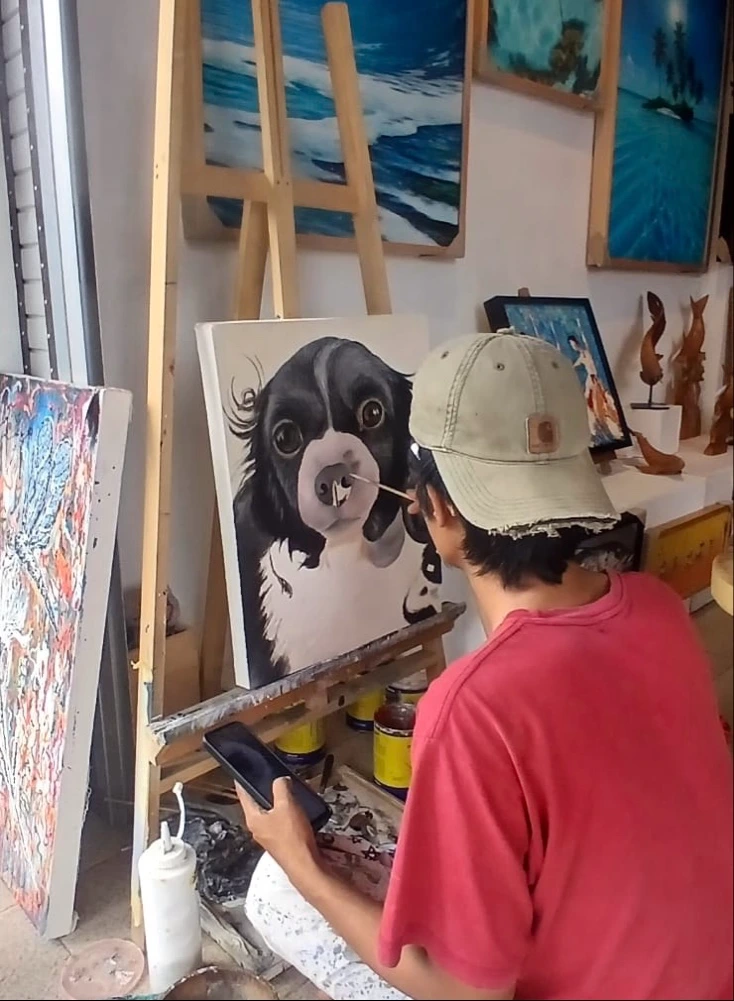 Alzen, hyperrealist portrait artist at Arts of Bali gallery Seminyak, working on a custom pet portrait painting of a dog using a smartphone reference photo