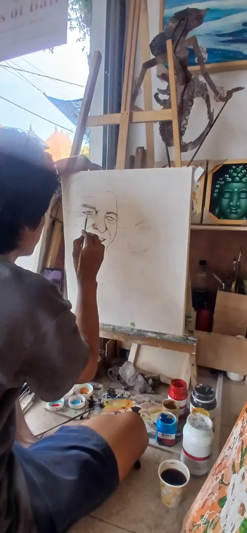 Bali portrait artist Alzen leaning close to the canvas to paint fine detail during a custom portrait commission at Arts of Bali gallery in Seminyak