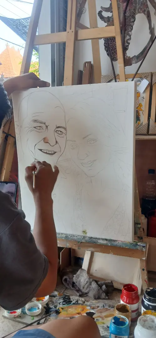 A Balinese portrait artist drawing the pencil outline of a commissioned portrait on canvas at Arts of Bali studio in Seminyak, the first stage of creating an oil painting from a photo in Bali