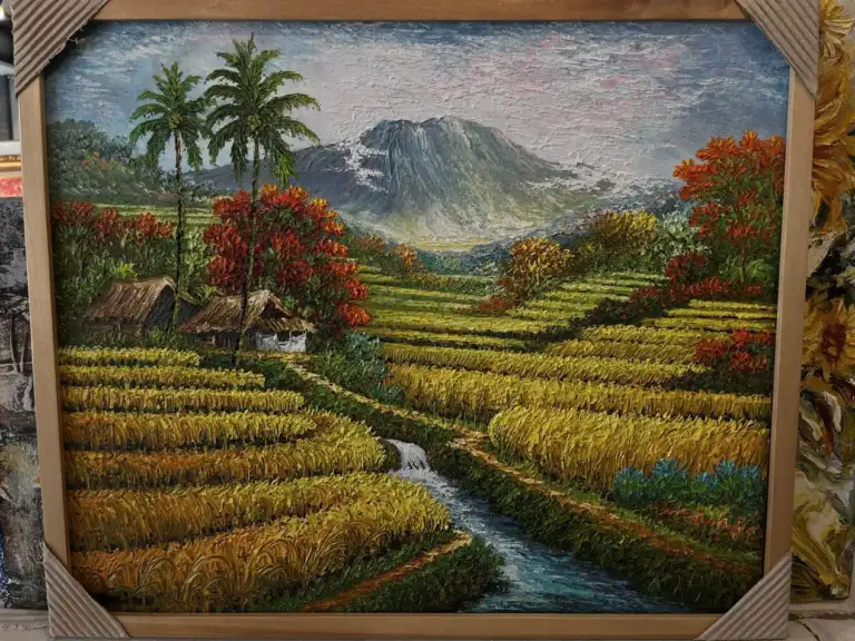 Highly textured Bali landscape painting showing terraced rice paddies, a tall coconut palm tree, a large flamboyant tree with red-orange foliage, and a grey volcanic mountain under a pale yellow sky.