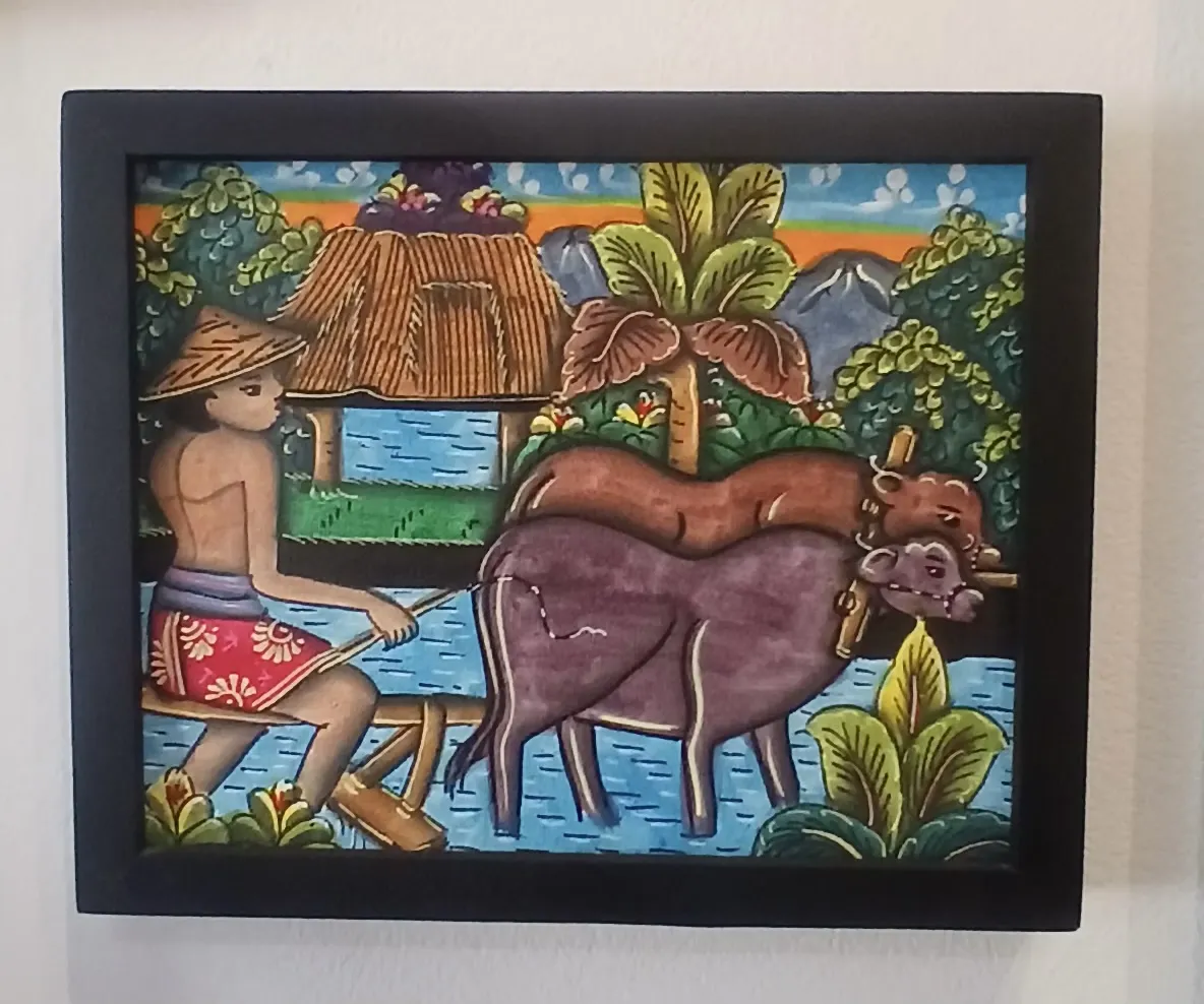 Batuan painting Bali of a Balinese farmer guiding two water buffaloes through flooded rice fields with a thatched-roof village hut and tropical trees in the background