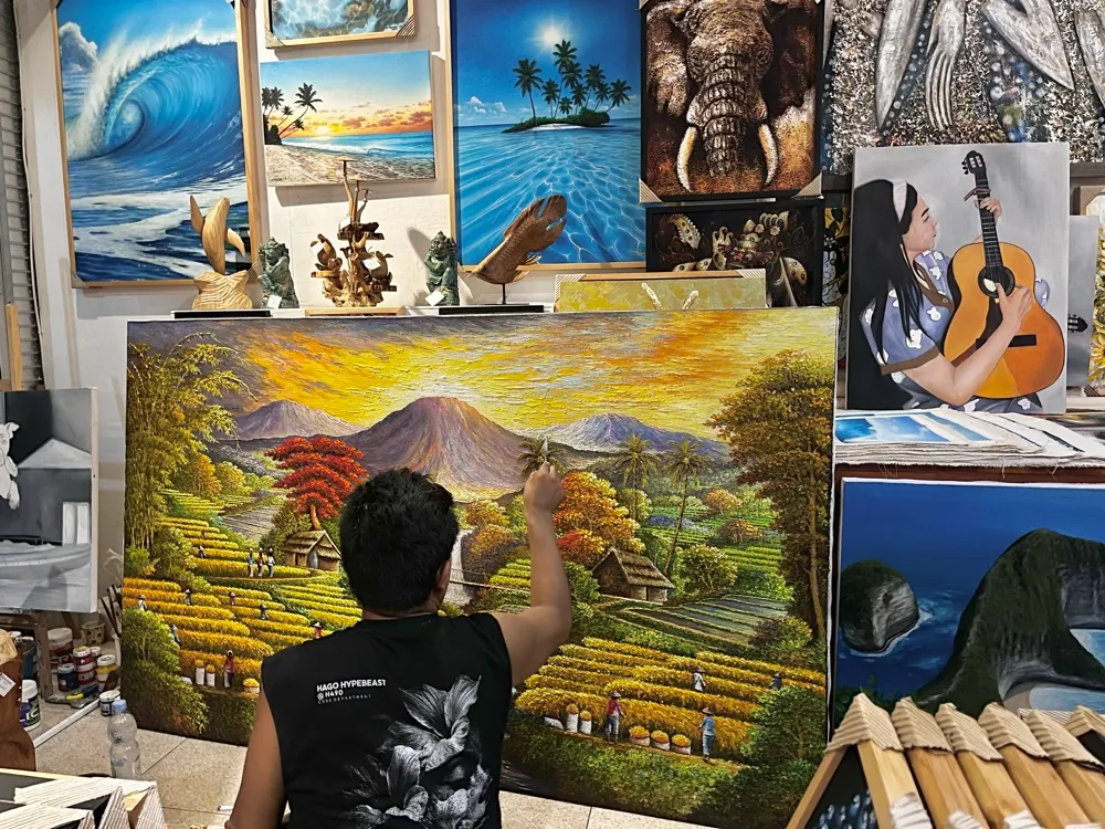 Gandara, Balinese landscape painter at Arts of Bali gallery Seminyak, working on a large canvas depicting Bali rice terraces and Mount Agung under a golden sunset sky