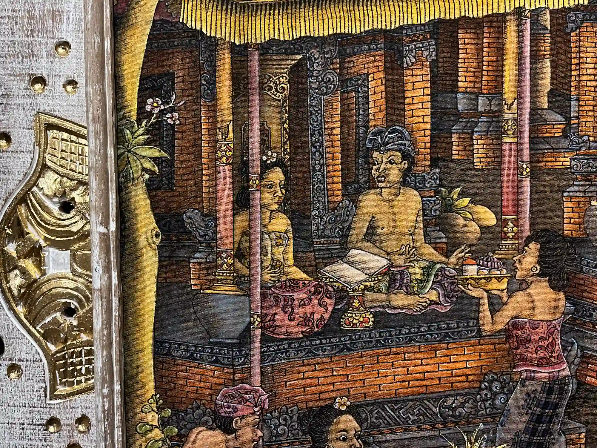Close-up detail of the classic Ubud style Balinese village life painting showing a Balinese nobleman reading a lontar palm leaf manuscript on an elevated bale, with a woman seated behind him and another presenting an offering tray, set within a traditional brick compound with carved columns