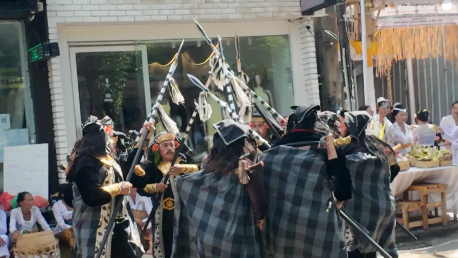 Group of Baris Gede male warrior performers in traditional black and white poleng checked sacred cloth holding ceremonial spear-like instruments during an Odalan ceremony on Jl. Raya Seminyak Bali