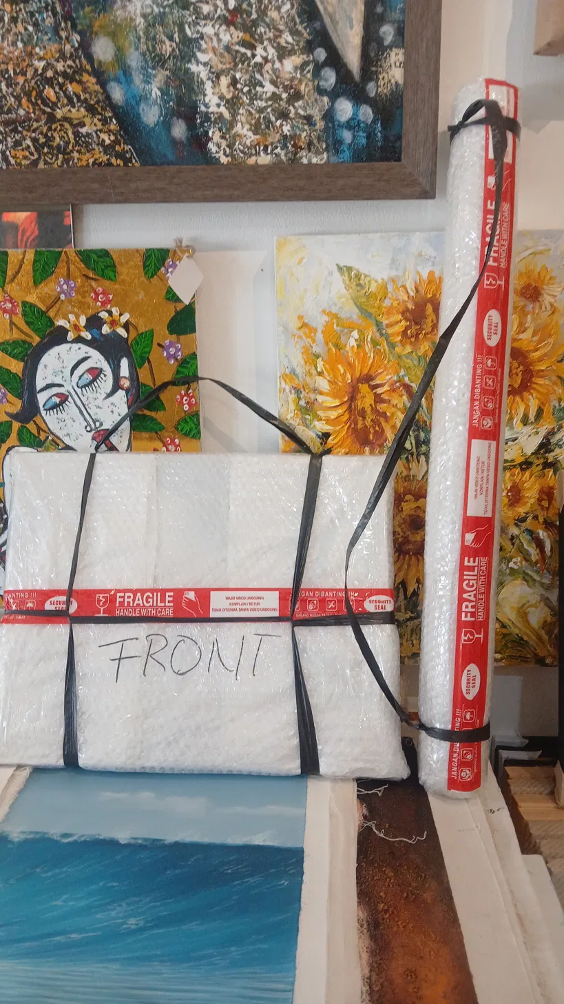 International Shipping Packaging for Original Paintings from Arts of Bali Two Arts of Bali shipping formats side by side: a foam-wrapped framed canvas secured with FRAGILE tape on the left, and a sealed PVC shipping tube for rolled canvases on the right