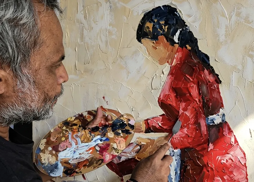 Balinese painter Upeksa holding colour palette working on figurative palette knife painting of Balinese woman in red at Arts of Bali gallery Seminyak Bali