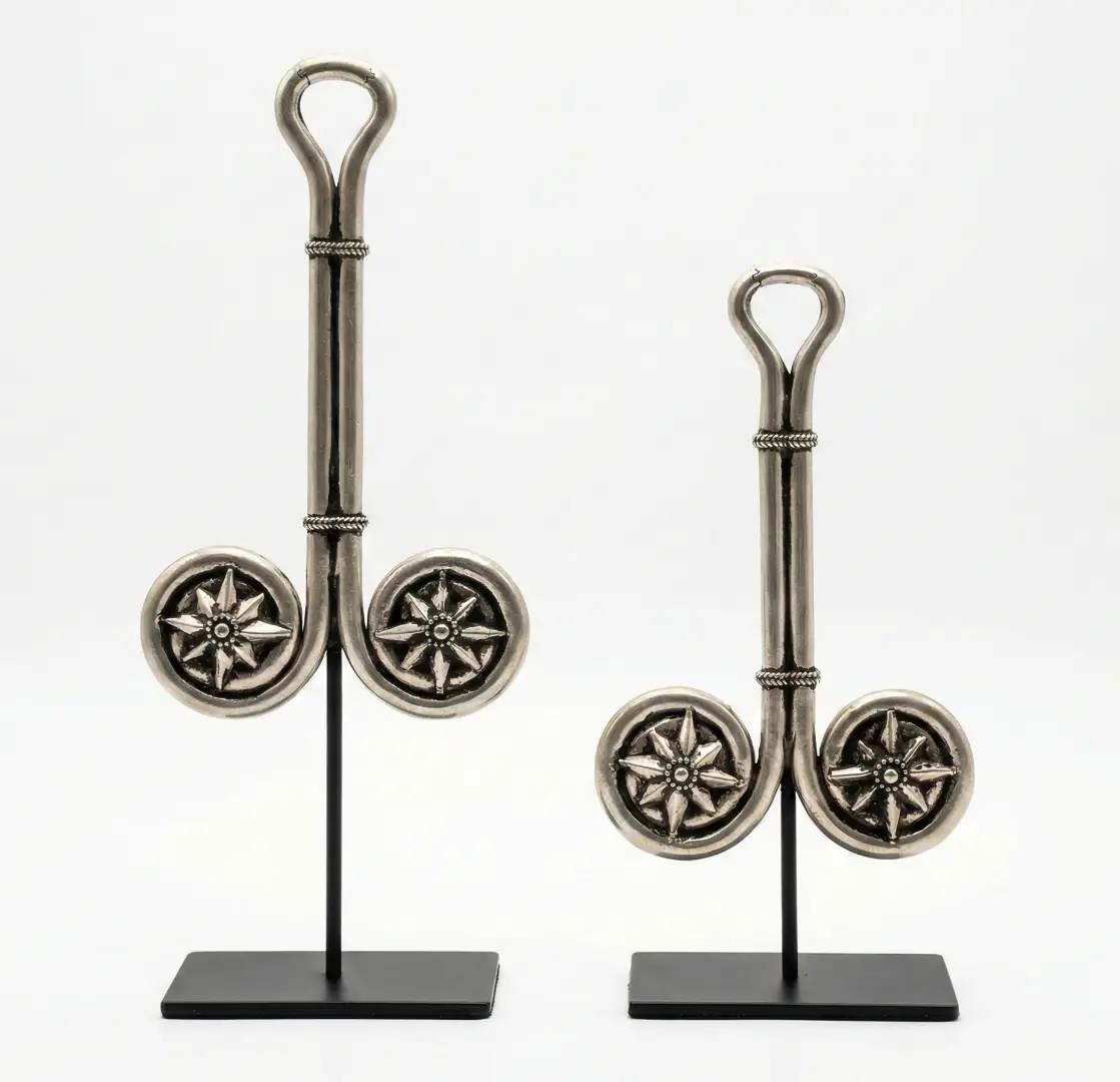 Pair of matching silver Balinese ceremonial objects each with a straight handle terminating in a loop at top and two circular disc medallions engraved with eight-pointed star motifs at base, mounted on black iron stands — sacred Indonesian metal art Arts of Bali Seminyak