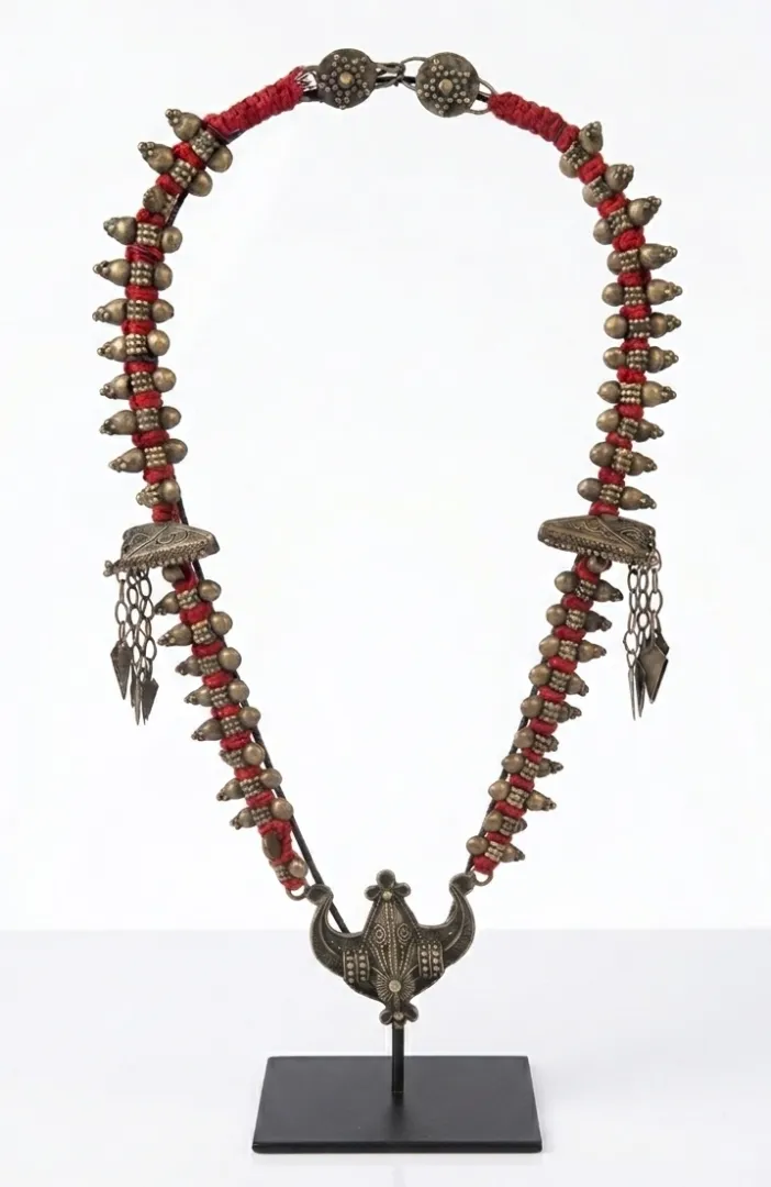 Traditional Eastern Indonesian tribal necklace with bronze torpedo-shaped beads on crimson red cord, crescent moon pendant with lotus motif at centre, triangular chain pendants at sides — antique Indonesian jewelry Arts of Bali Seminyak