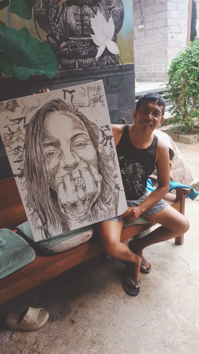Artist at Arts of Bali Seminyak holding the in-progress portrait commission canvas during underdrawing phase