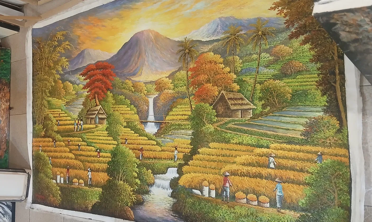 Large textured oil painting of Balinese rice field terraces with a central volcano under a dramatic orange and yellow sunset sky, waterfall, traditional huts, and palm trees, displayed at Arts of Bali gallery Seminyak