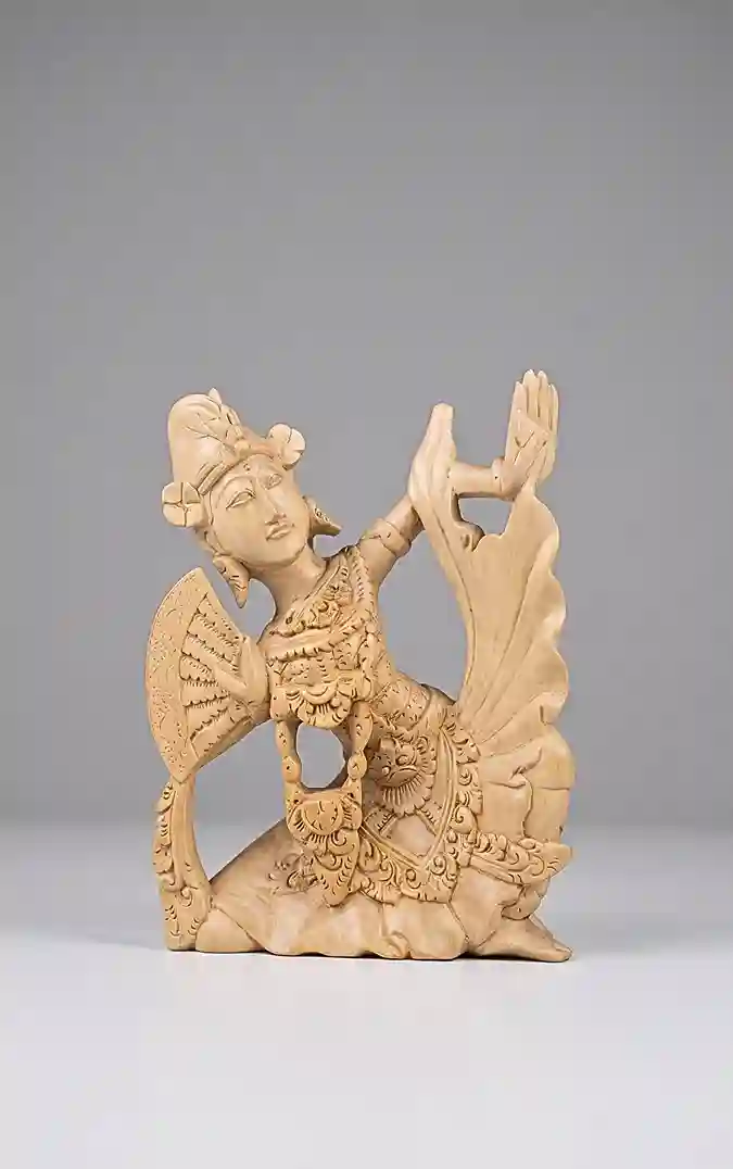 Balinese wood carving of Tari Kebyar Duduk seated dancer with right hand raised in mudra palm-outward gesture, detailed costume with fan elements, natural light wood tone on grey background, Arts of Bali Seminyak
