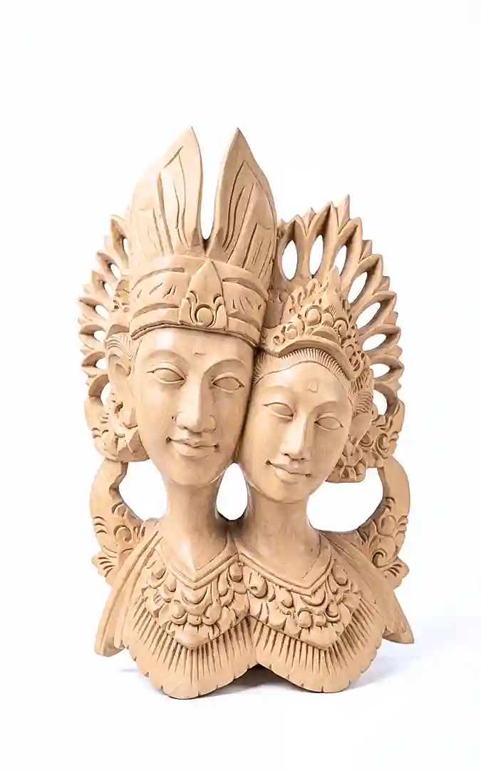 Balinese wood carving of pengantin wedding couple as joined double bust, male figure with tall pointed mahkota crown and female with rounder floral headdress, both facing slightly apart, natural warm wood on white background, Arts of Bali