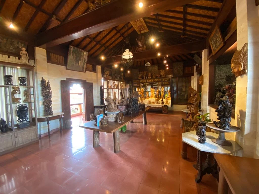 Interior of the Njana Tilem Museum showing carved wooden sculptures displayed under a traditional joglo roof, Mas village