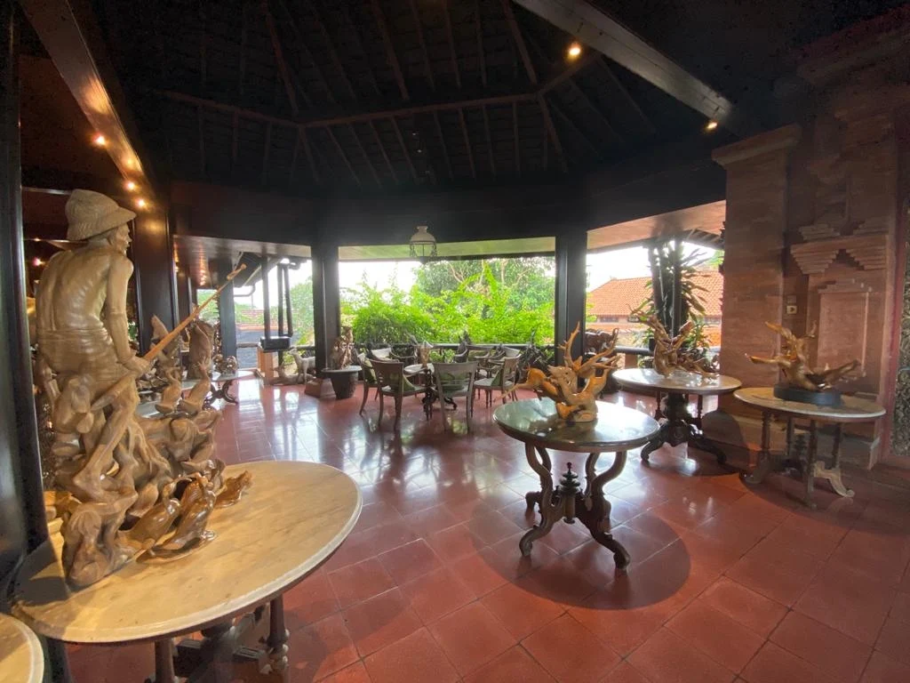 Open-air veranda at the Njana Tilem Museum with carved wooden sculptures and a garden view, Mas village, Gianyar
