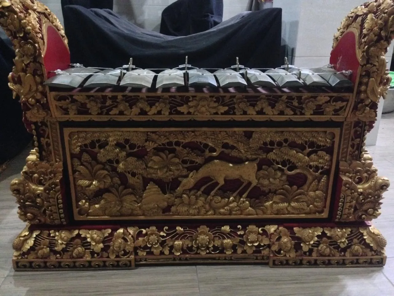 Balinese gamelan metallophone with a row of metal keys above a carved gold and red wooden frame
