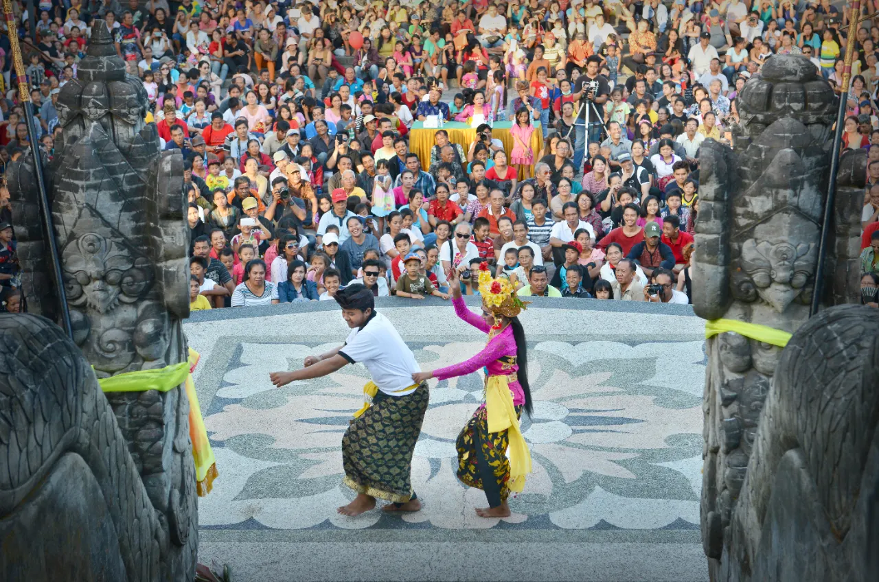 A couple dancing Joged Bumbung in front of a split gate with a large crowd watching in Bali