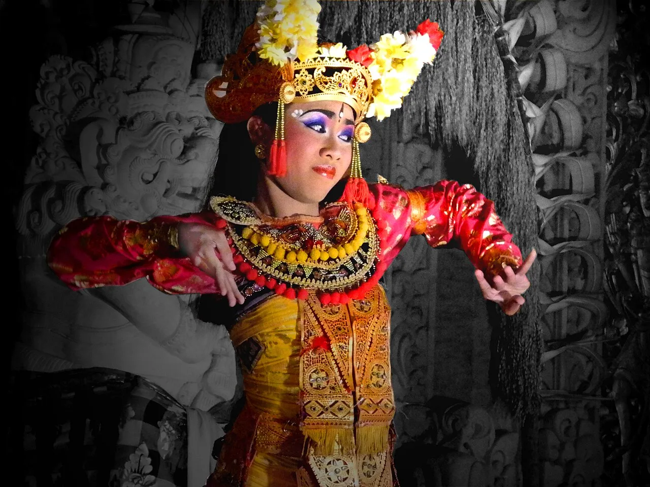 Young legong dance performer in a flower headdress and red costume in mid-movement in Ubud, Bali