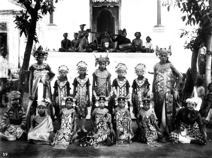 Historic group portrait of legong dancers in costume with a gamelan ensemble behind them in Bali